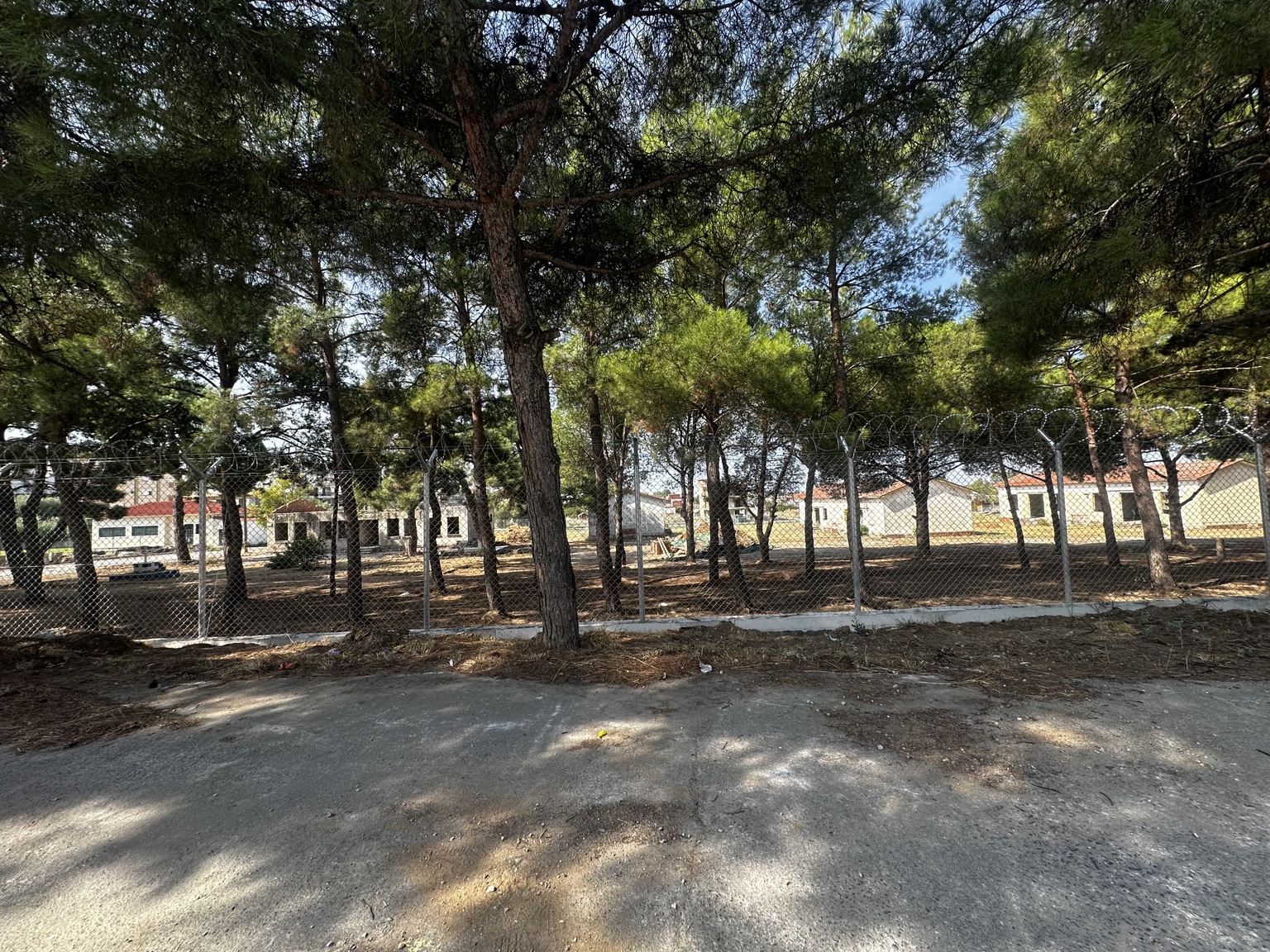 Η περίφραξη και τα κτίρια του πρώην στρατοπέδου ανάμεσα στα δέντρα